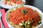 A Plate Of Spaghetti Topped With A Rich Arrabbiata Sauce And Garnished With Fresh Basil, Accompanied By Sautéed Zucchini, Served On A Modern Table Setting.