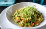 A vibrant bowl of spring risotto with pea, garnished with finely grated cheese and fresh herbs, ready to be savored.