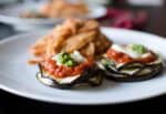 Elegant Vegan Grilled Eggplant Stacks Layered With Cheese And Topped With Rich Tomato Sauce And A Dollop Of Pesto, Served With A Side Of Pasta.