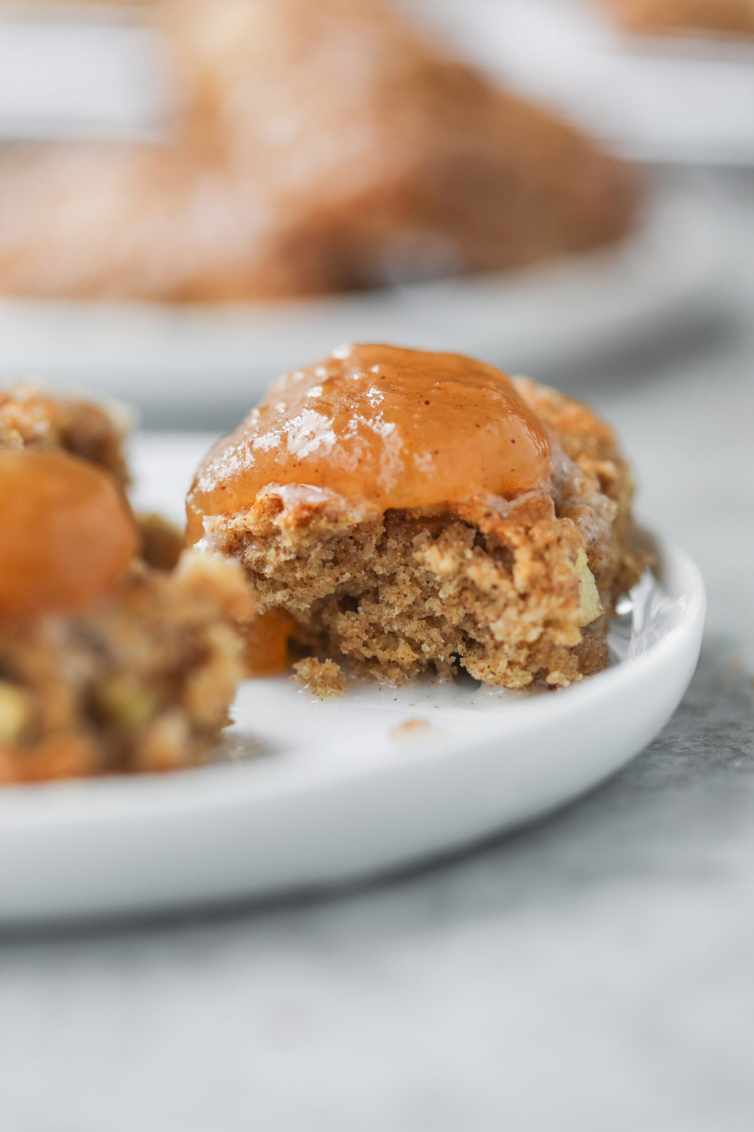 A Close-Up Of A Spiced Cake Or Cookie Topped With Glossy Caramel Sauce And A Generous Layer Of Apple Butter Sits On A White Plate, With A Bite Taken Out, Showing Its Moist Interior.