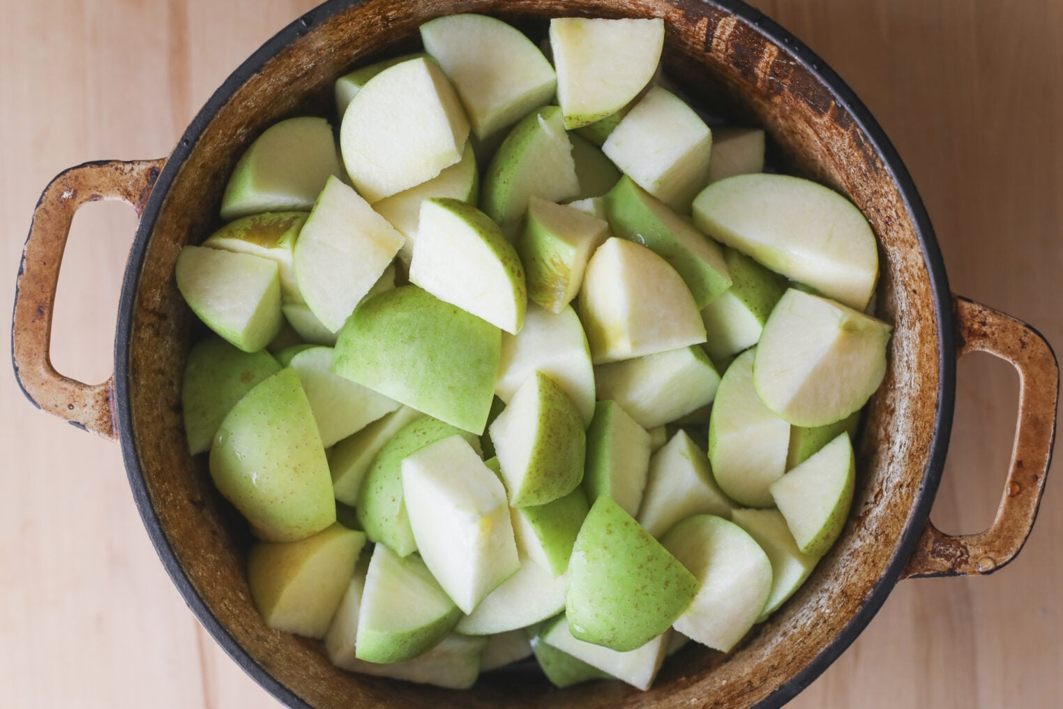 A Top-Down View Of A Rustic Pot Filled With Freshly Chopped Green Apple Pieces, Perfect For Making Homemade Apple Butter, Sitting On A Wooden Surface.