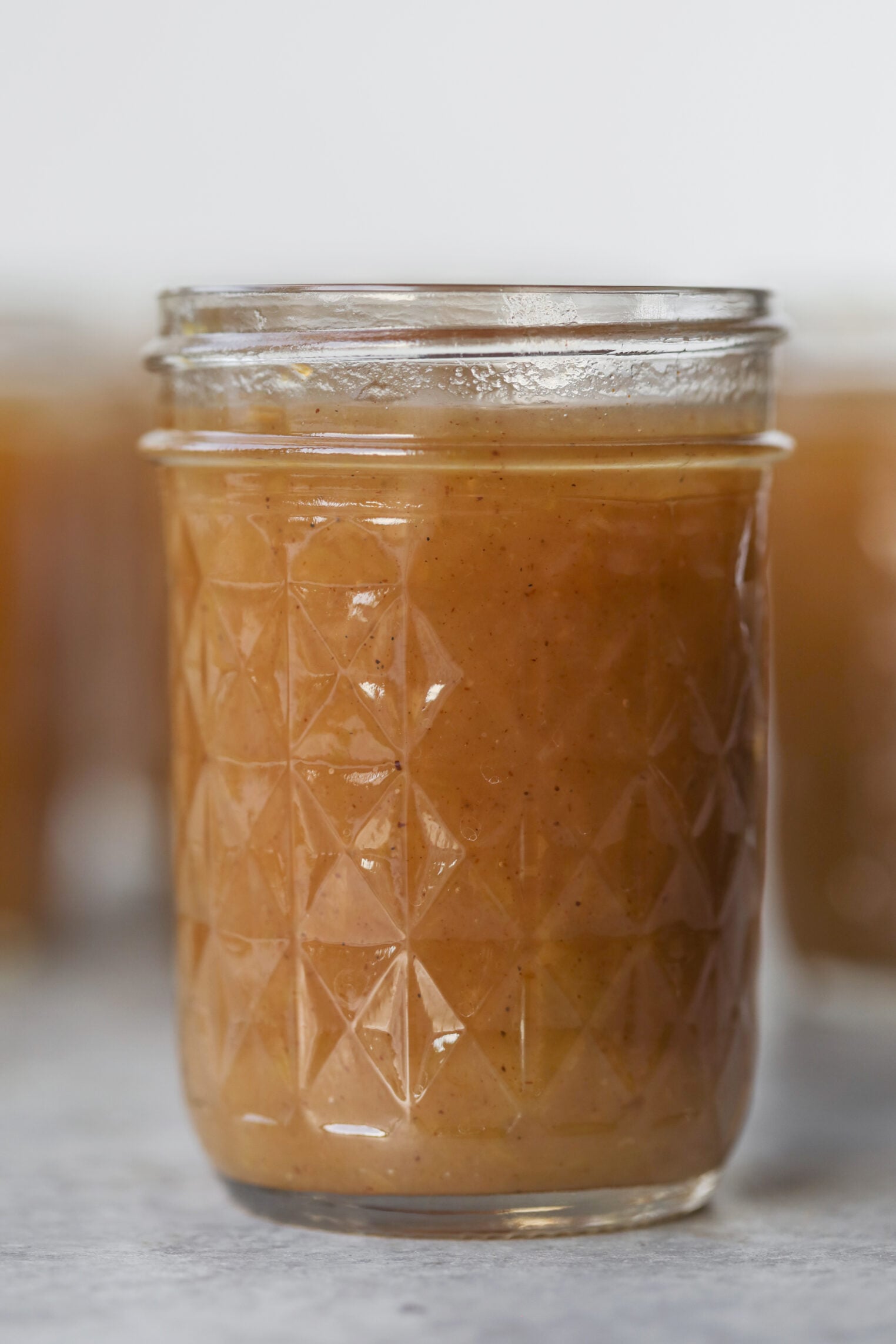 A Close-Up Of A Glass Jar Filled With Light Brown Caramel Sauce, Featuring A Diamond-Patterned Texture On The Jar. The Sauce Appears Smooth And Glossy, Reminiscent Of Rich Apple Butter In Both Color And Sheen.