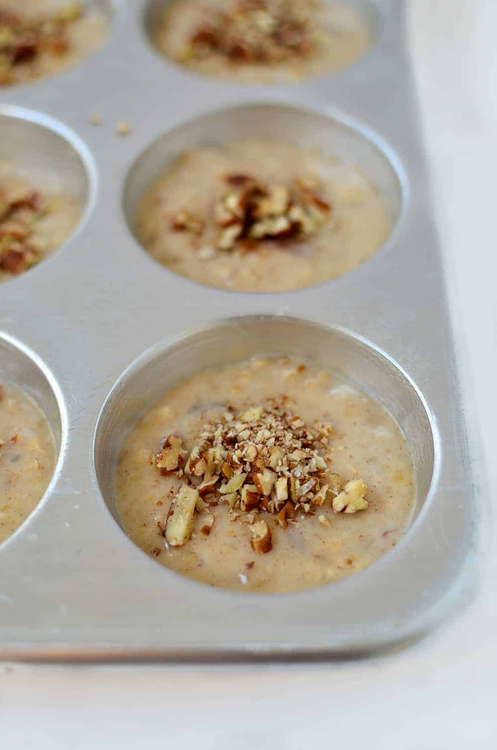 Unbaked muffin batter in the muffin pan with some crushed pecan nuts