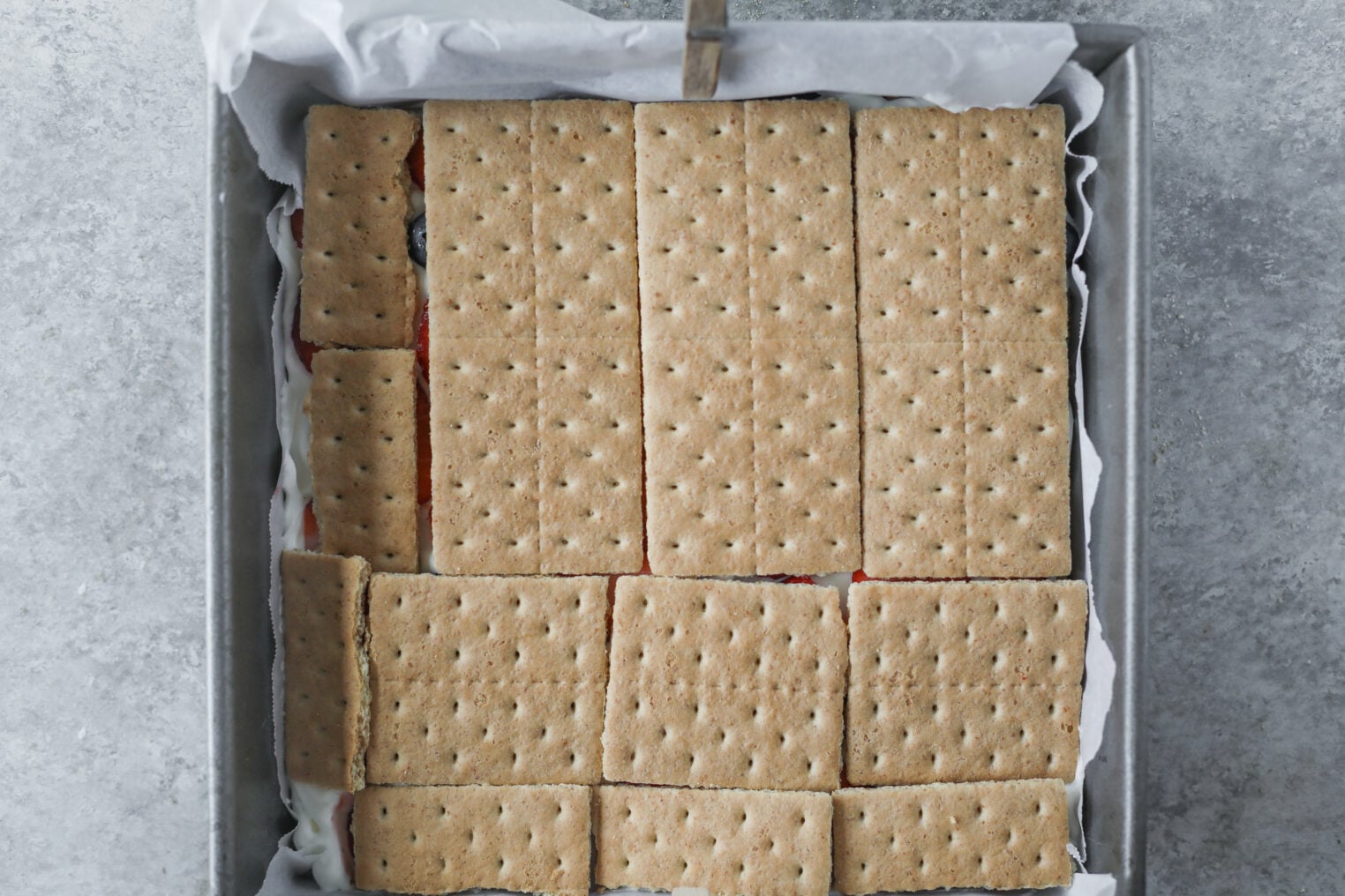 Berry Icebox Cake 7 A Square Baking Pan Lined With Parchment Paper, Filled With A Layer Of Rectangular Graham Crackers Covering A Berry Icebox Cake Dessert.