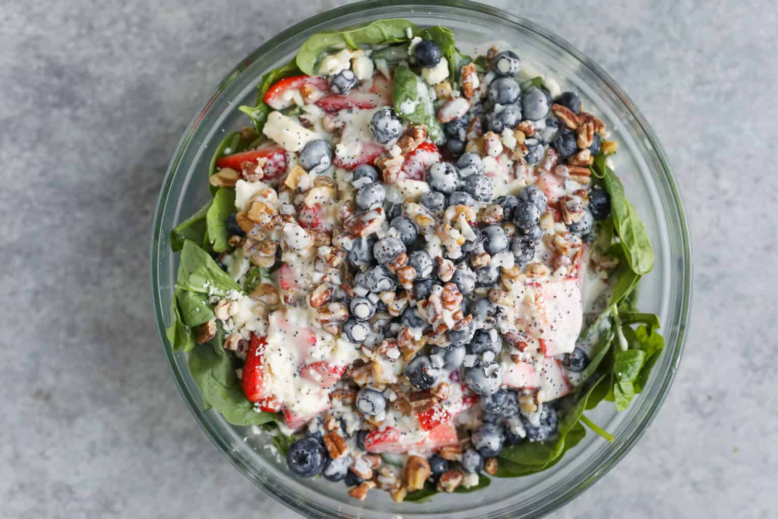 Strawberry Poppyseed Salad 5 A Glass Bowl Filled With A Vibrant Strawberry Poppy Seed Salad—Fresh Spinach Topped With Sliced Strawberries, Blueberries, Chopped Nuts, Crumbled Cheese, And Creamy Dressing—Set On A Gray Surface.