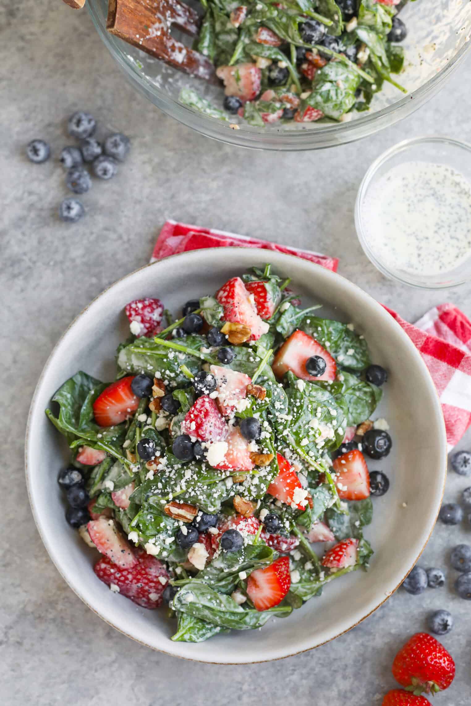 Strawberry Poppyseed Salad 6 A Vibrant Strawberry Poppy Seed Salad Features Spinach, Strawberries, Blueberries, Crumbled Cheese, And Chopped Nuts With A Creamy Dressing. Nearby, A Glass Bowl Of Salad, Loose Berries, And A Jar Of Dressing Rest On A Gray Surface.