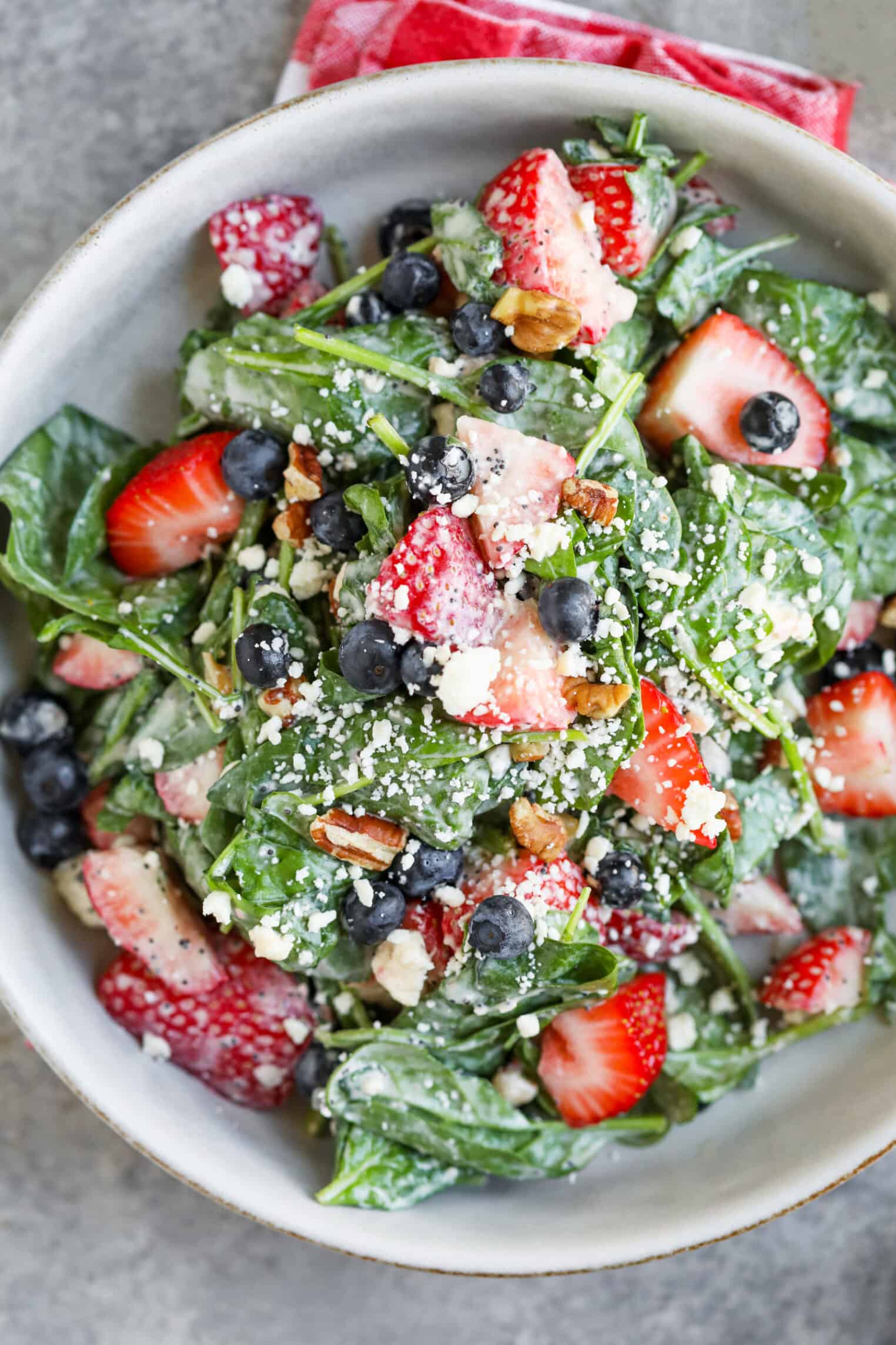 Strawberry Poppyseed Salad 1 A Bowl Of Fresh Strawberry Salad With Spinach, Blueberries, Pecans, And Crumbled Cheese, Lightly Dressed—Perfect For A Poppy Seed Twist—On A Gray Surface With A Red Napkin Partially Visible.