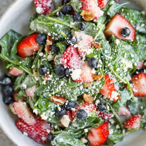 Strawberry Poppyseed Salad 9 A Bowl Of Fresh Strawberry Salad With Spinach, Blueberries, Pecans, And Crumbled Cheese, Lightly Dressed—Perfect For A Poppy Seed Twist—On A Gray Surface With A Red Napkin Partially Visible.