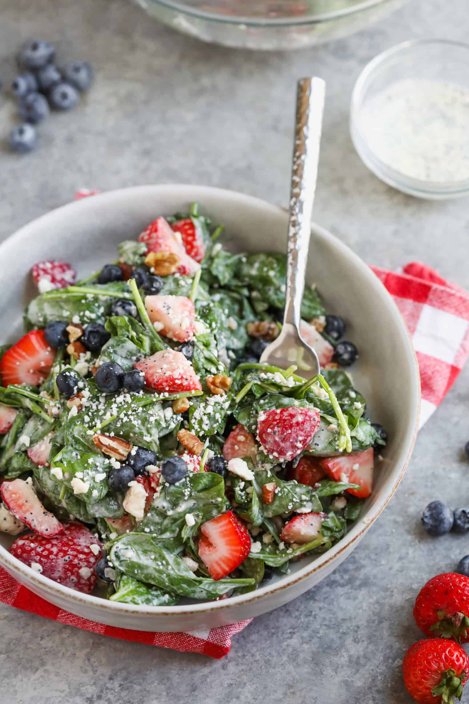 Strawberry Poppyseed Salad 3 A Bowl Of Fresh Spinach Strawberry Poppyseed Salad With Blueberries, Chopped Nuts, And Crumbled Cheese Sits On A Gray Surface With A Fork. A Red Plaid Napkin, Loose Berries, And Salad Dressing Are Nearby.