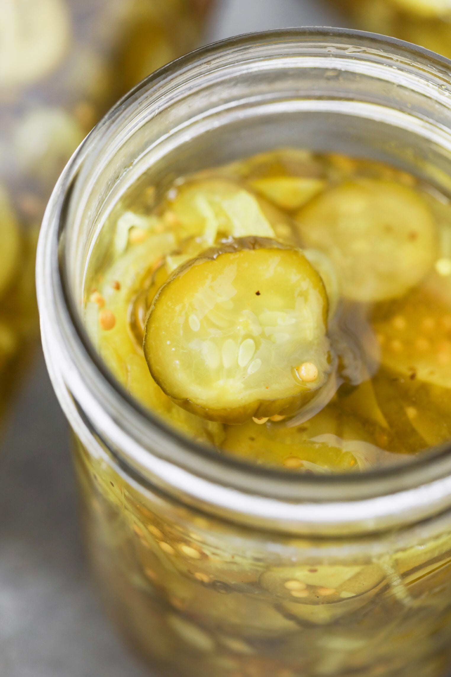 A Close-Up Of A Glass Jar Filled With Sliced Bread And Butter Pickles In Brine, Showing The Details Of The Pickle Slices And Seeds.