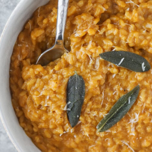 Butternut Squash Risotto 9 A Bowl Of Creamy Butternut Squash Risotto Topped With Three Sage Leaves And Grated Cheese, With A Spoon Resting In The Risotto.