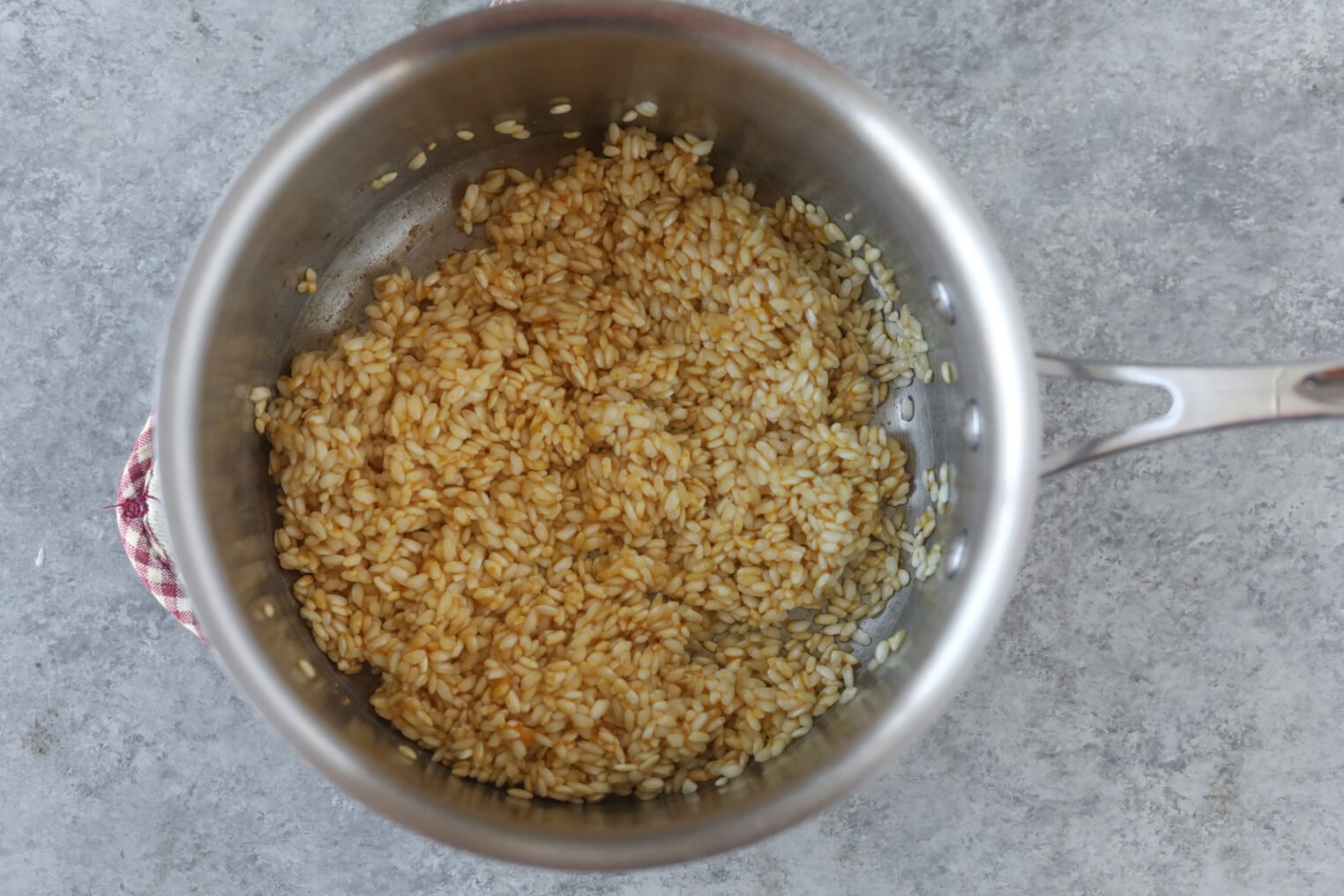 Butternut Squash Risotto 5 A Stainless Steel Pot Filled With Uncooked Arborio Rice Coated In A Light Brown Liquid, Ready To Become Creamy Butternut Squash Risotto, Sits On A Gray Countertop.