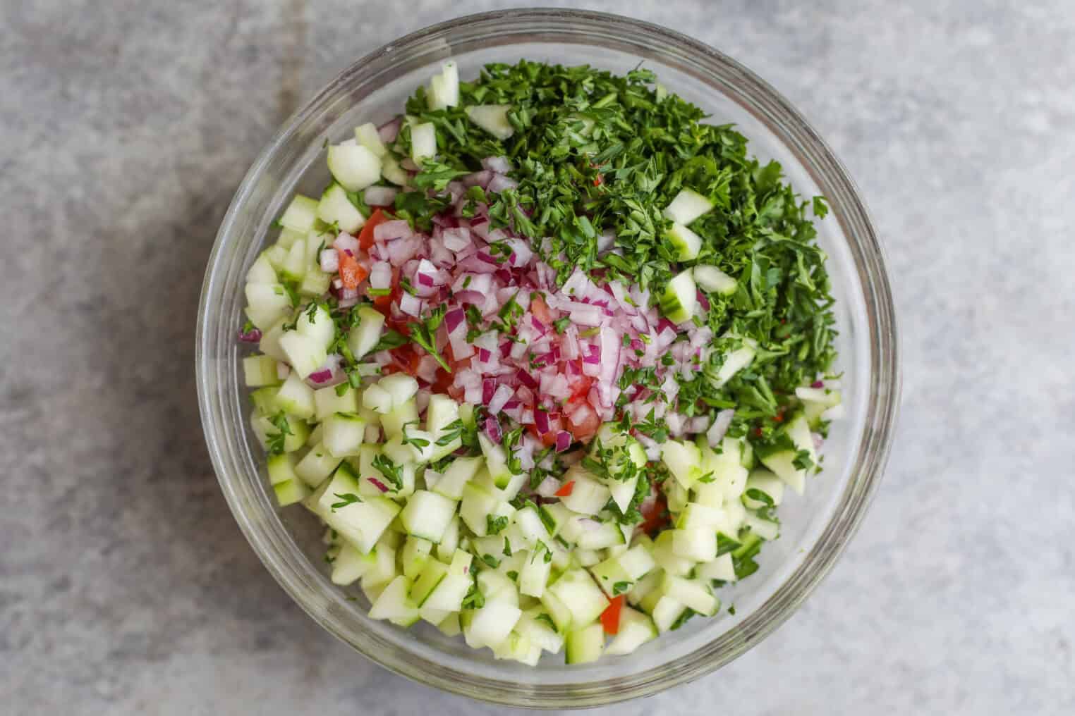 Cauliflower Shawarma 6 A Glass Bowl Filled With Chopped Cucumber, Red Onion, Tomato, And Fresh Parsley—Perfect For Serving Alongside Flavorful Cauliflower Shawarma—Arranged In Separate Sections On A Gray Surface.