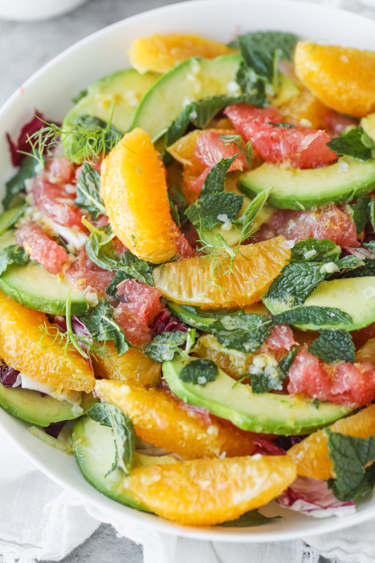 A Fresh Salad Featuring Orange And Grapefruit Segments, Avocado Slices, Fresh Mint Leaves, And Mixed Greens In A White Bowl.