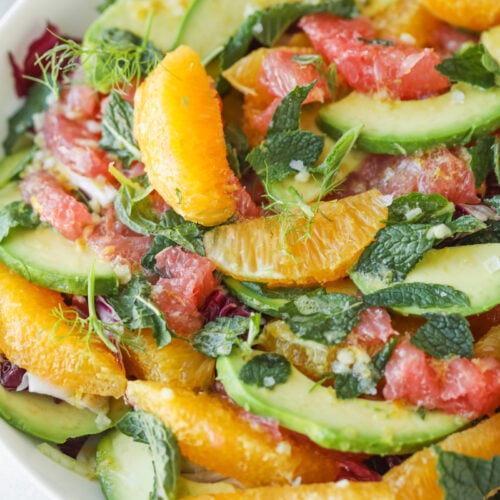 A Fresh Salad Featuring Orange And Grapefruit Segments, Avocado Slices, Fresh Mint Leaves, And Mixed Greens In A White Bowl.