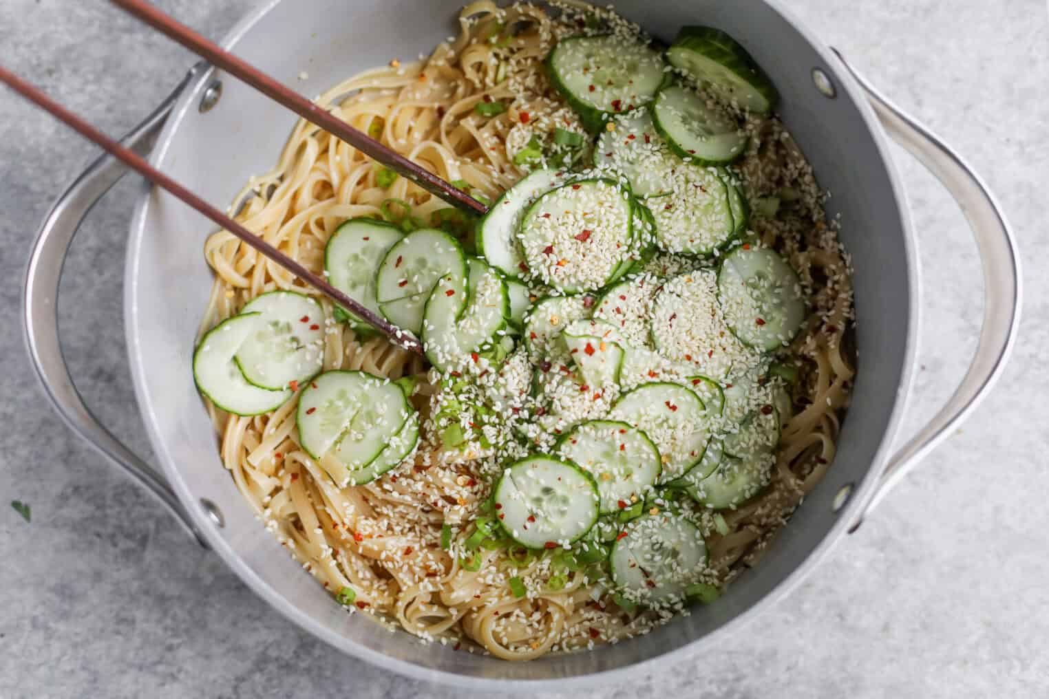 Cold Sesame Noodles With Cucumbers 7 A Pot Of Cold Sesame Noodles Topped With Sliced Cucumbers, Sesame Seeds, And Red Pepper Flakes, With A Pair Of Chopsticks Resting In The Pot.