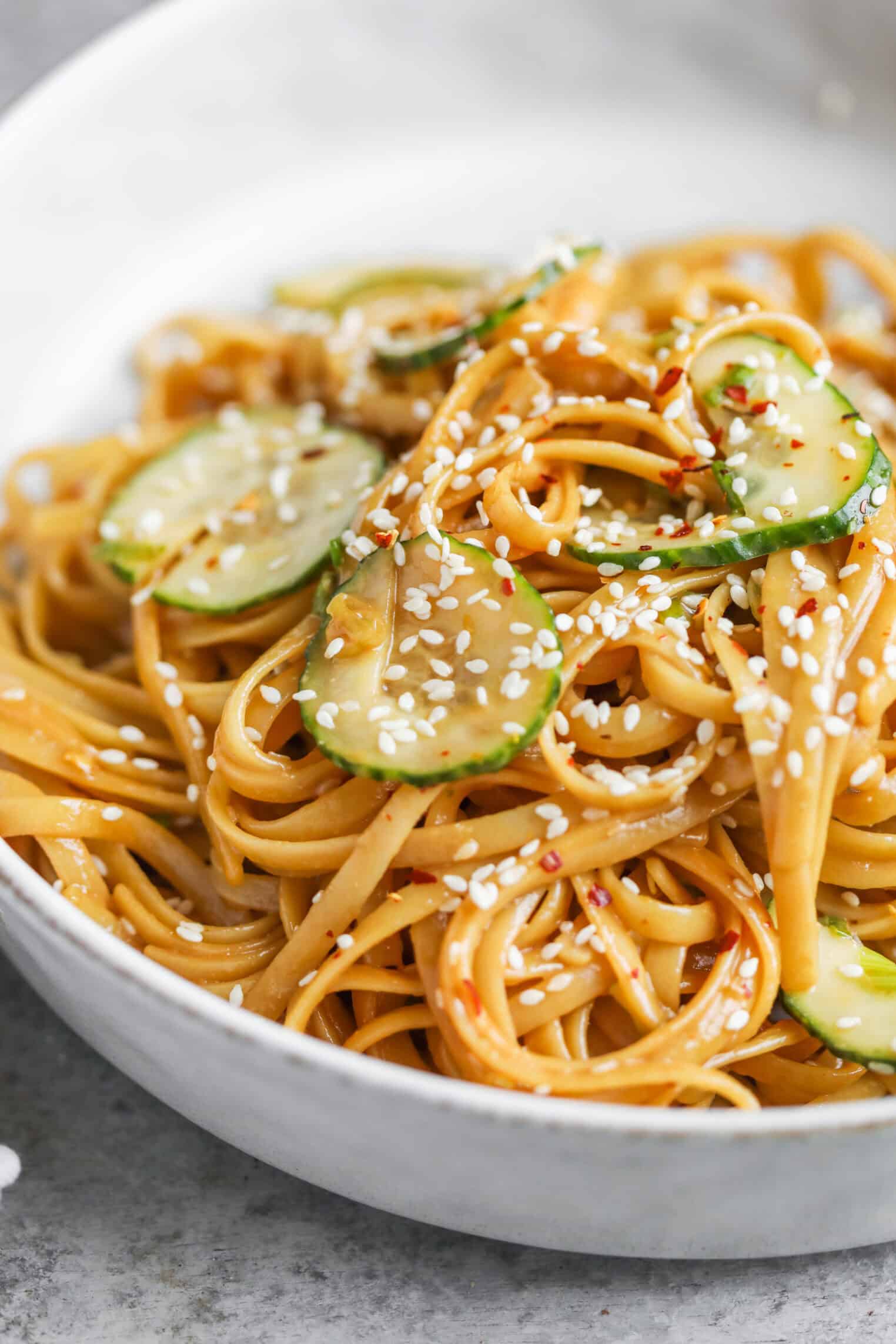 Cold Sesame Noodles With Cucumbers 1 A Close-Up Of Cold Sesame Noodles Topped With Sliced Cucumbers, Sesame Seeds, And A Light Sauce, Served In A White Bowl.