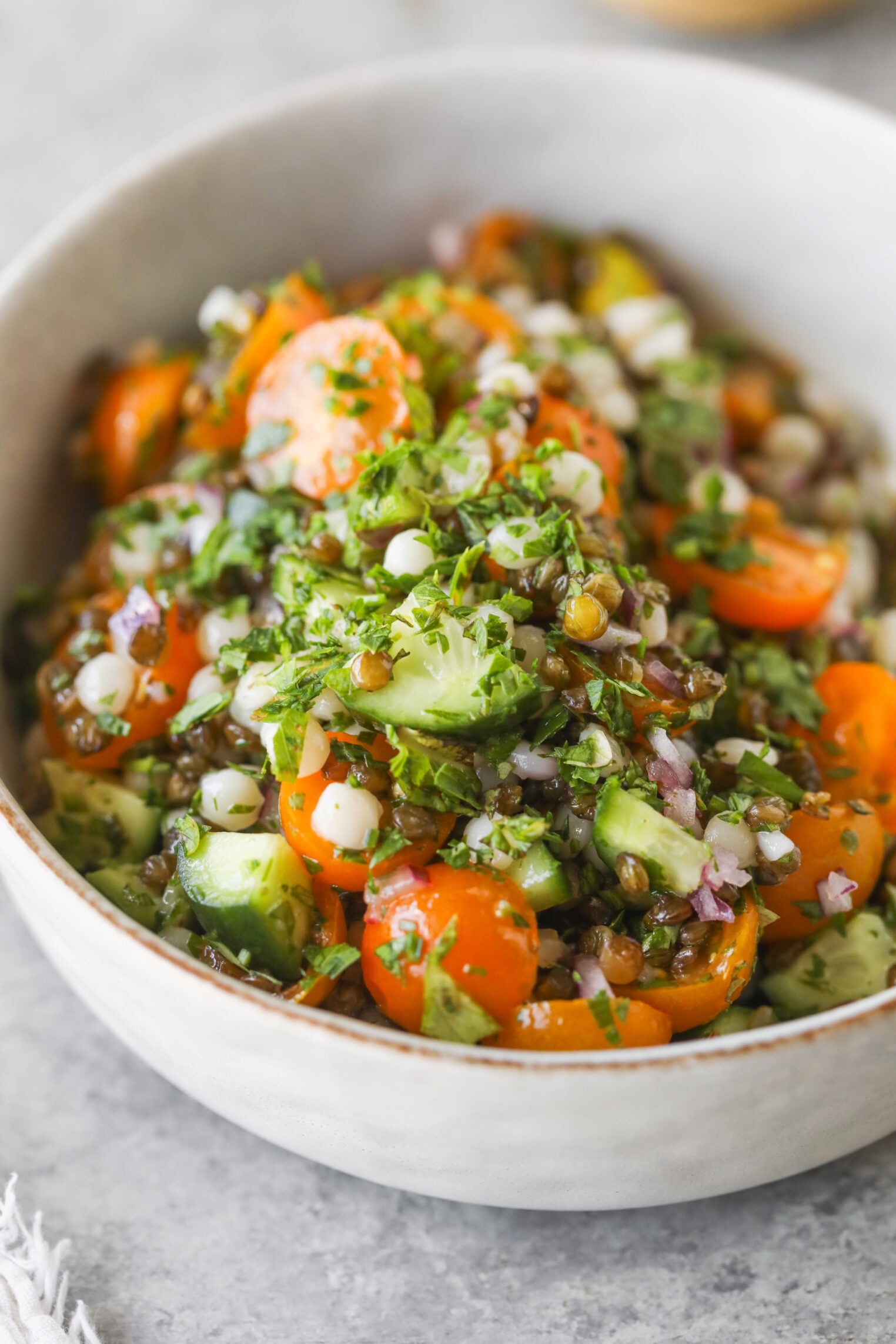 A Bowl Of Fresh Salad With Chopped Cucumbers, Cherry Tomatoes, Red Onions, Parsley, And Green Lentils Comes Together In A Delicious Lentil Tabbouleh Style, All Mixed Together And Garnished With Herbs.