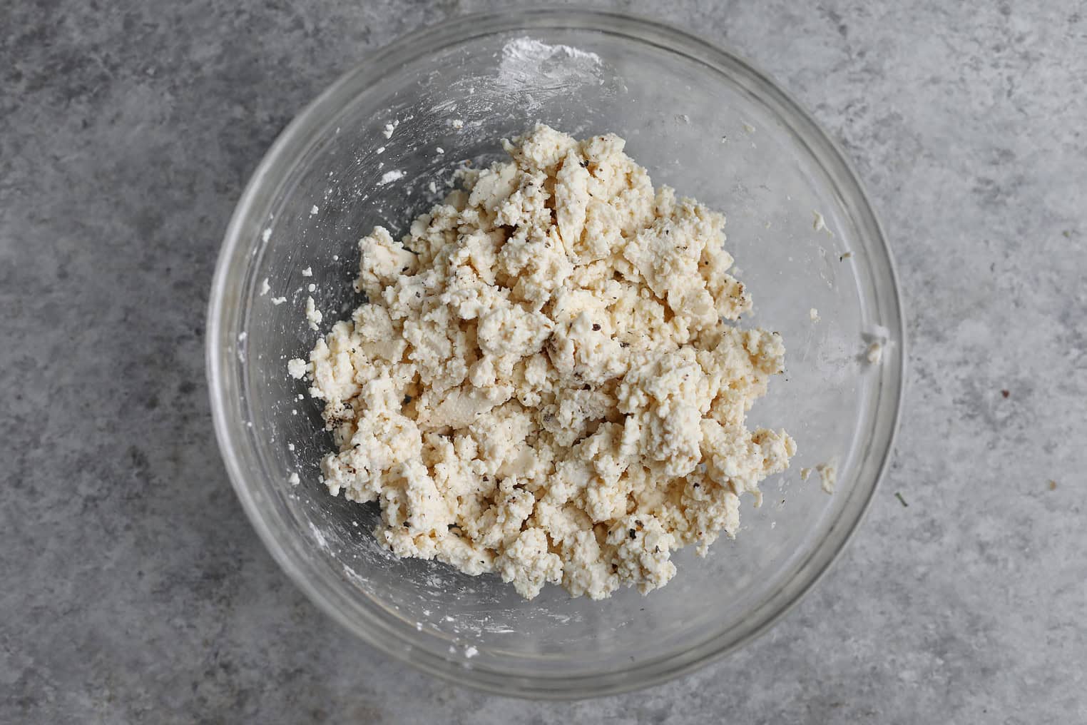 Crispy Quinoa Salad 6 A Clear Glass Bowl Containing A Mixture Of Crumbly, Pale Dough Sits On A Gray, Textured Surface, Reminiscent Of The Fresh Ingredients Often Found In A Crispy Quinoa Salad.