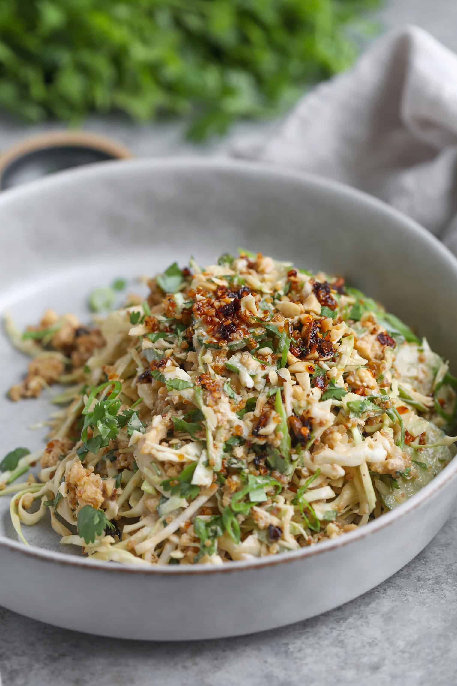 Crispy Quinoa Salad 3 A Bowl Of Noodles Topped With Ground Meat, Chopped Herbs, And A Generous Drizzle Of Chili Oil, Served Alongside A Crispy Quinoa Salad On A Light Gray Plate With A Soft Napkin And Fresh Greens In The Background.