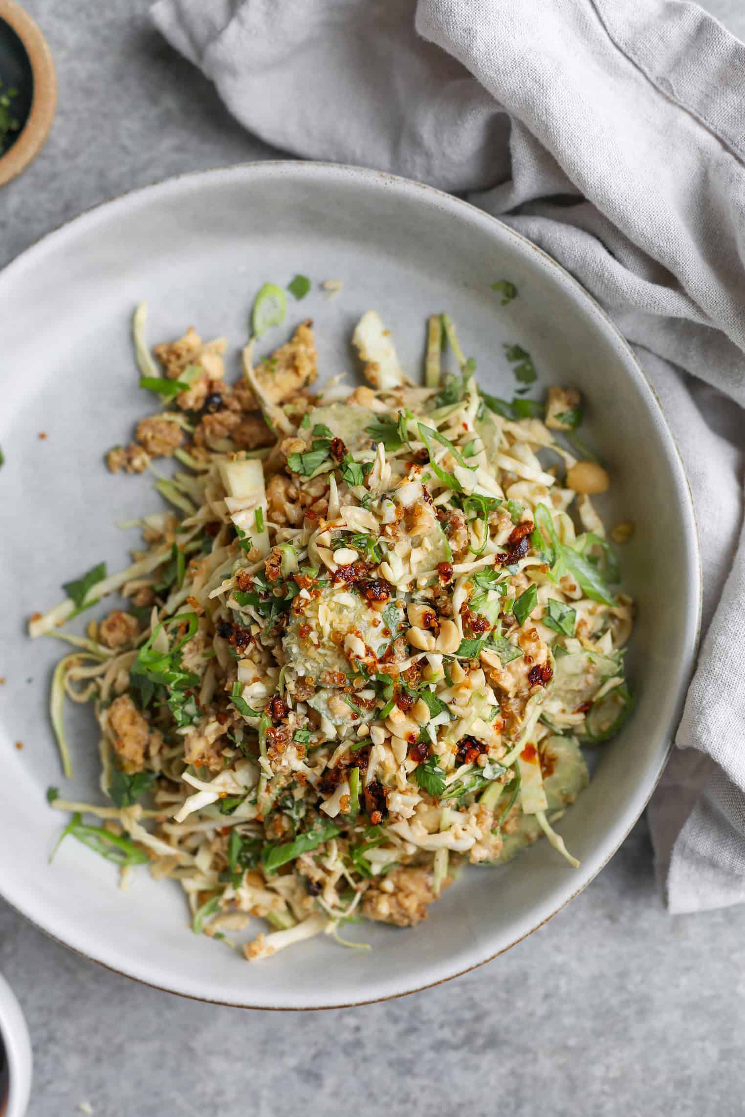 Crispy Quinoa Salad 11 A Plate Of Noodle Salad Topped With Chopped Herbs, Peanuts, And Crumbled Tofu Sits On A Light Gray Surface With A Beige Napkin Beside It, Reminiscent Of A Vibrant Crispy Quinoa Salad.