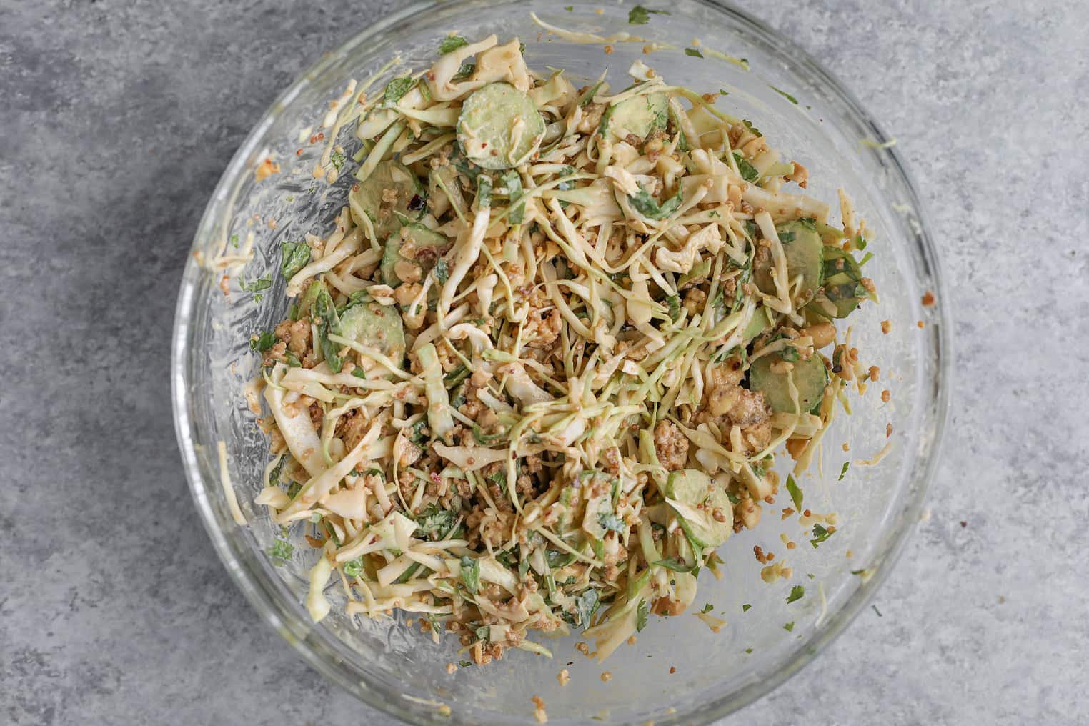 Crispy Quinoa Salad 9 A Glass Bowl Filled With A Fresh Crispy Quinoa Salad, Blending Cabbage, Sliced Cucumbers, Herbs, And Crunchy Toppings On A Gray Textured Surface.