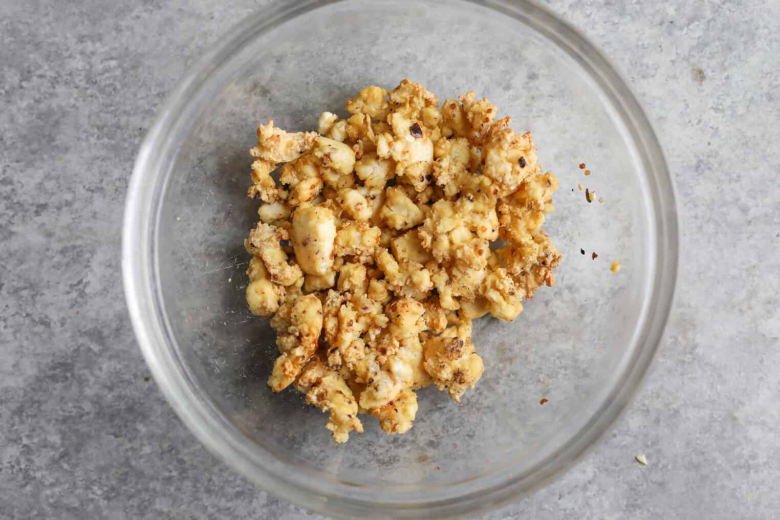 Crispy Quinoa Salad 7 A Clear Glass Bowl On A Grey Surface Containing Seasoned, Cooked Cauliflower Florets With Visible Spices—Perfect As A Topping For Your Crispy Quinoa Salad.