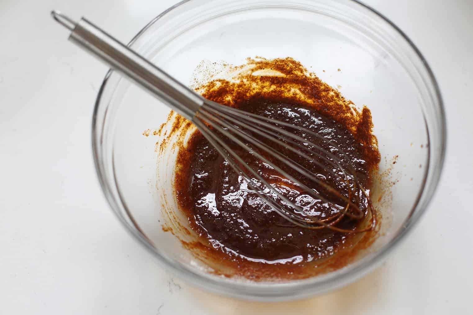 Crispy Tofu Tacos with Cashew Lime Crema 5 A Metal Whisk Rests In A Glass Bowl Filled With A Thick, Dark Brown Mixture On A White Surface, Perfect For Preparing Sauces For Crispy Tofu Tacos.