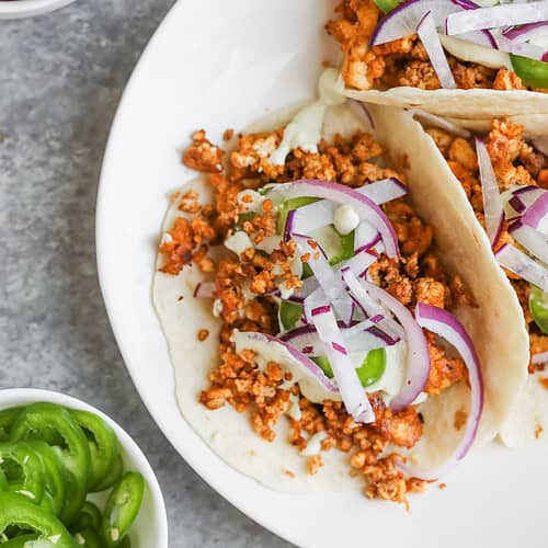 Crispy Tofu Tacos with Cashew Lime Crema 11 Three Crispy Tofu Tacos Filled With Seasoned Crumbled Tofu, Sliced Red Onions, And Green Bell Peppers On A White Plate. Nearby Are Small Bowls With Sliced JalapeƱos, Extra Tofu, And More Red Onions For Topping.