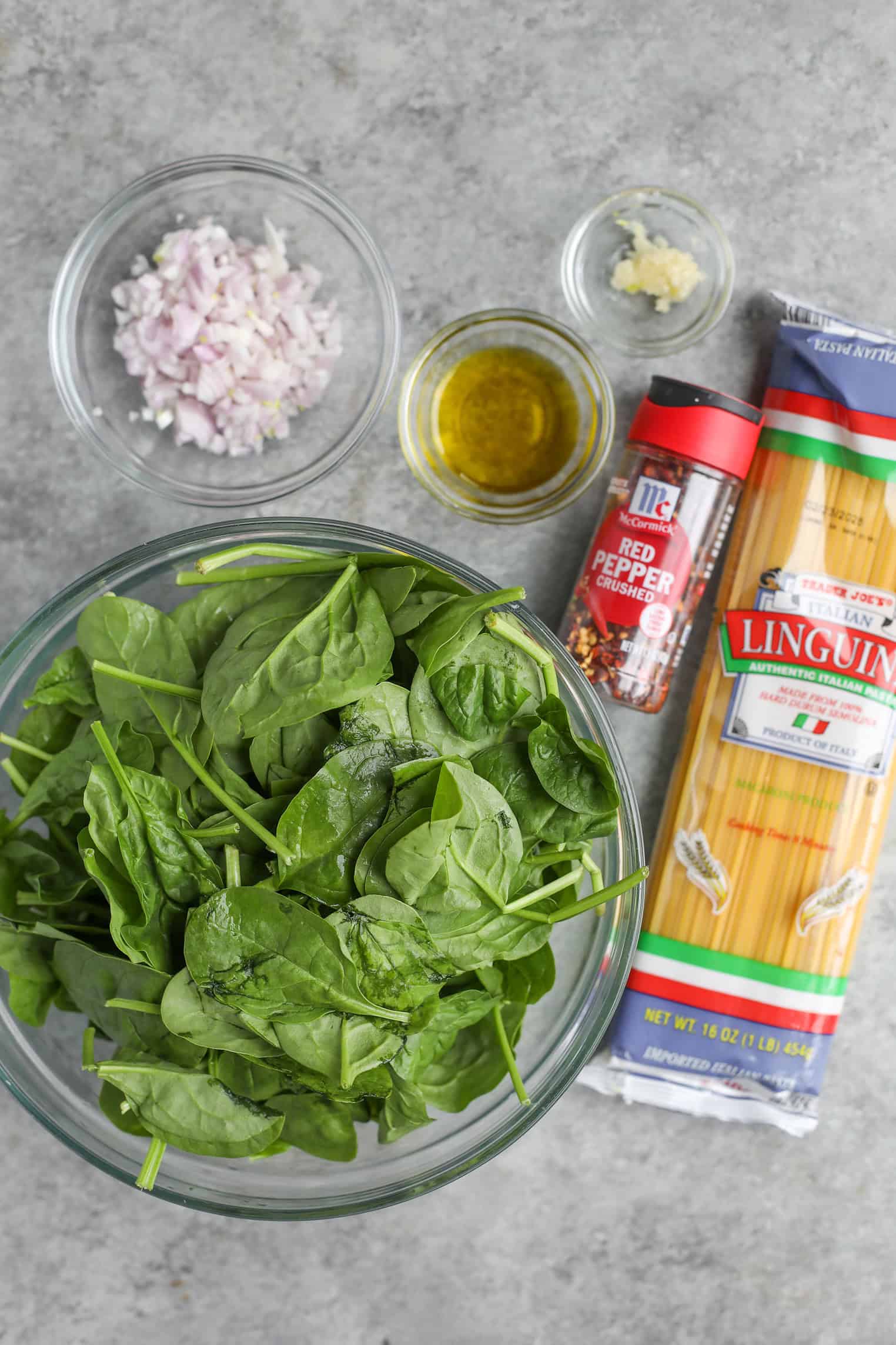 Easy Vegan Pasta 2 A Bowl Of Fresh Spinach, Chopped Shallots, Minced Garlic, Olive Oil, Red Pepper Flakes, And A Package Of Linguine Pasta Are Arranged On A Gray Countertop—Perfect For Creating A Vibrant Vegan Pasta Dish.