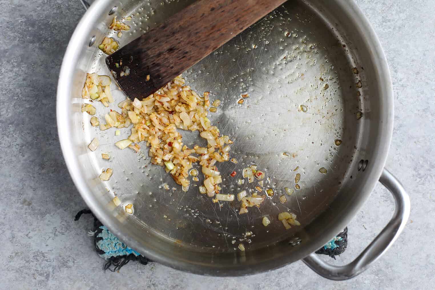 Easy Vegan Pasta 4 Chopped Onions Being Sautéed In A Stainless Steel Pot With A Wooden Spatula, Some Onions Are Browned While Others Are Still Softening In Oil—The Perfect Start For A Flavorful Vegan Pasta.