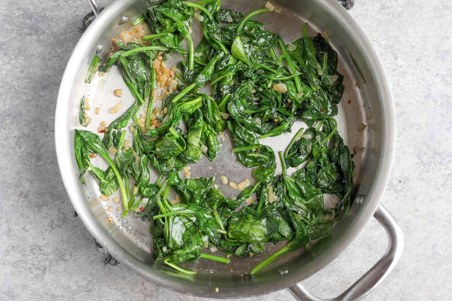 Easy Vegan Pasta 5 Sautéed Spinach And Diced Onions In A Stainless Steel Pan On A Gray Countertop, Perfect As A Flavorful Base For Vegan Pasta.