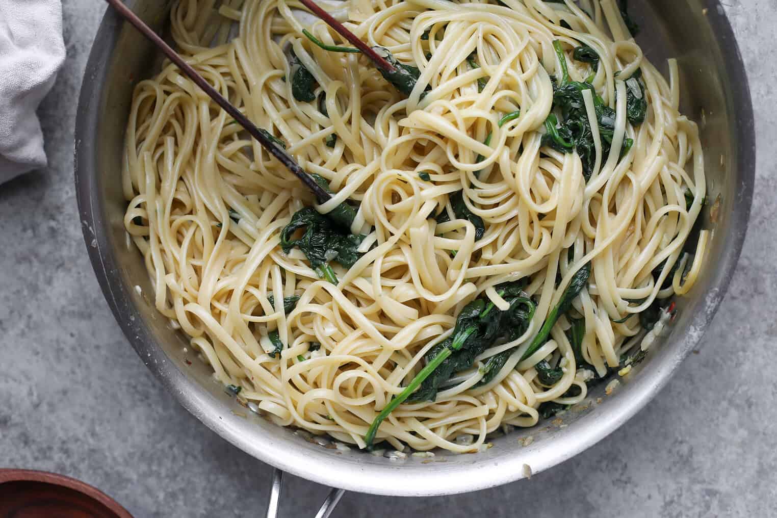 Easy Vegan Pasta 6 A Pan Of Cooked Vegan Pasta Mixed With Wilted Spinach, Tossed With Olive Oil And Seasonings, With Metal Tongs Resting Inside. The Background Is A Gray Countertop.
