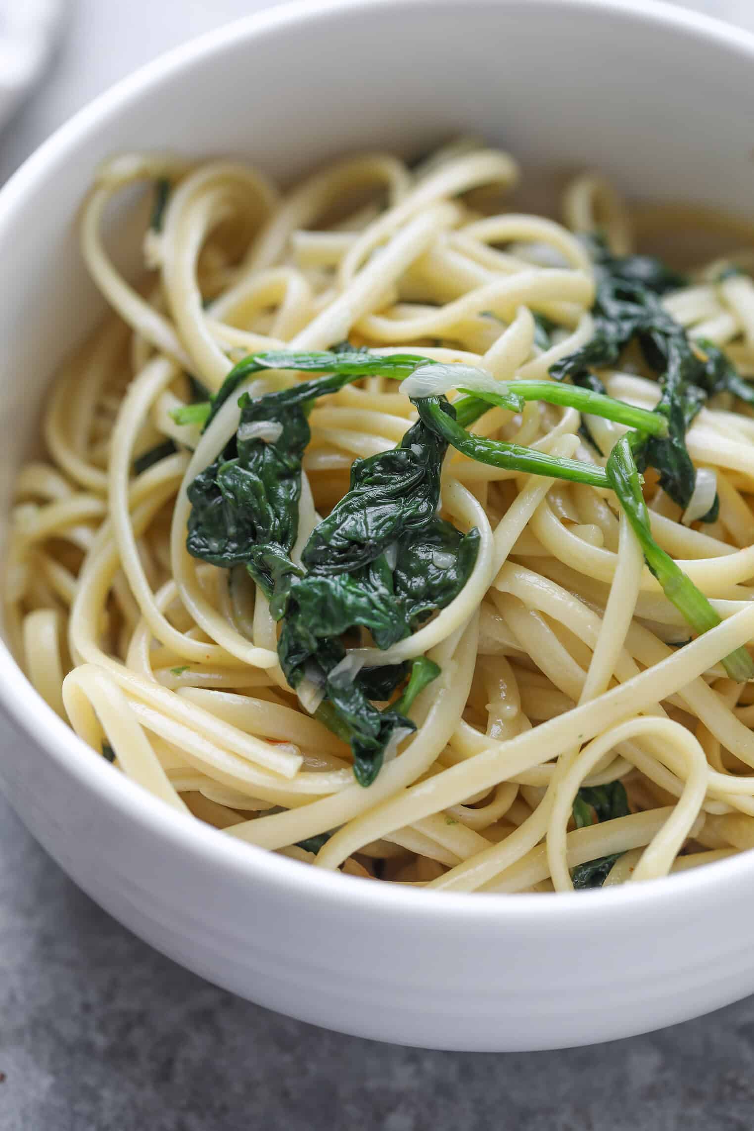 Easy Vegan Pasta 10 A White Bowl Filled With Vegan Pasta Linguine And Wilted Spinach, Placed On A Light Gray Surface.
