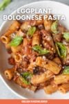 A plate of Eggplant Lentil Bolognese pasta with rigatoni, garnished with basil and sprinkled with grated cheese, with "Eggplant Lentil Bolognese pasta