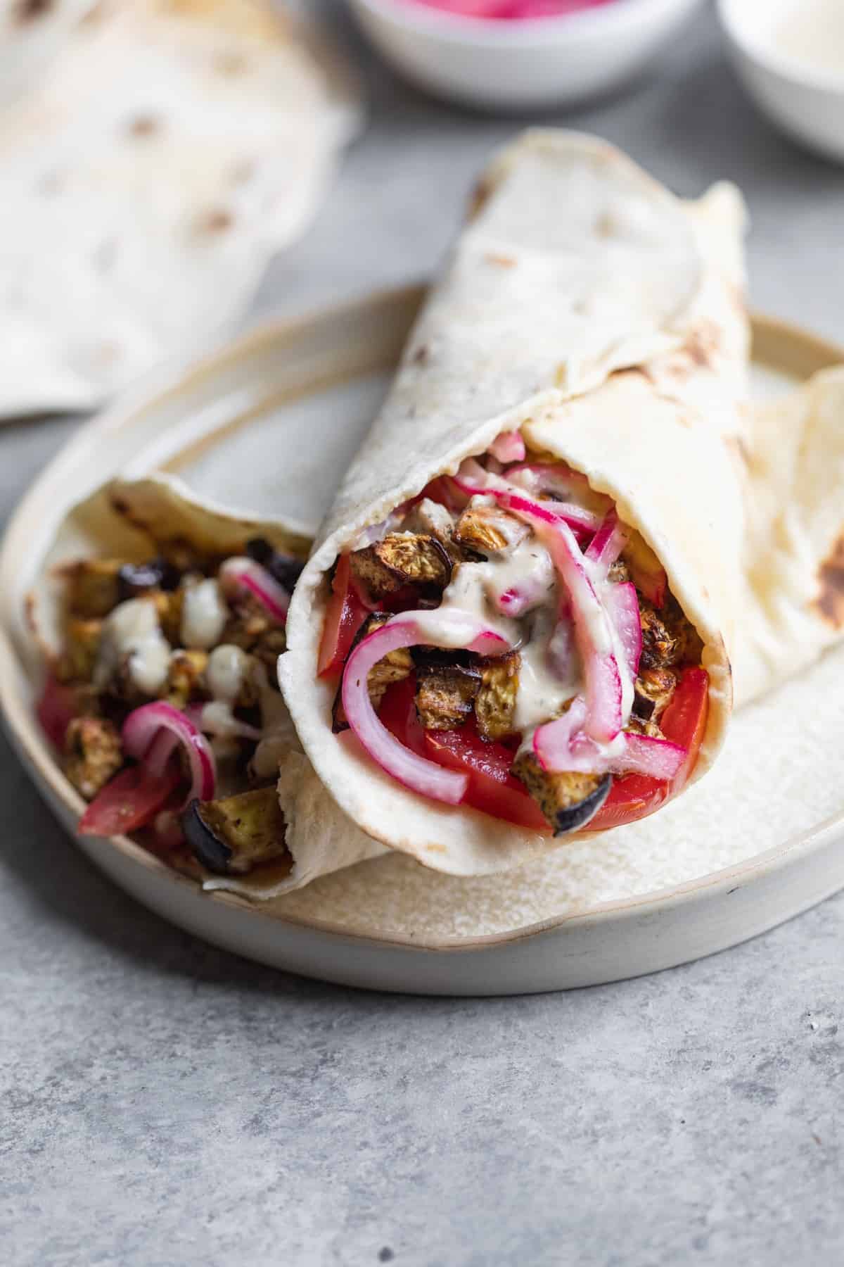 Two Vegan Eggplant Gyros Stacked With Pickled Red Onions And Hummus