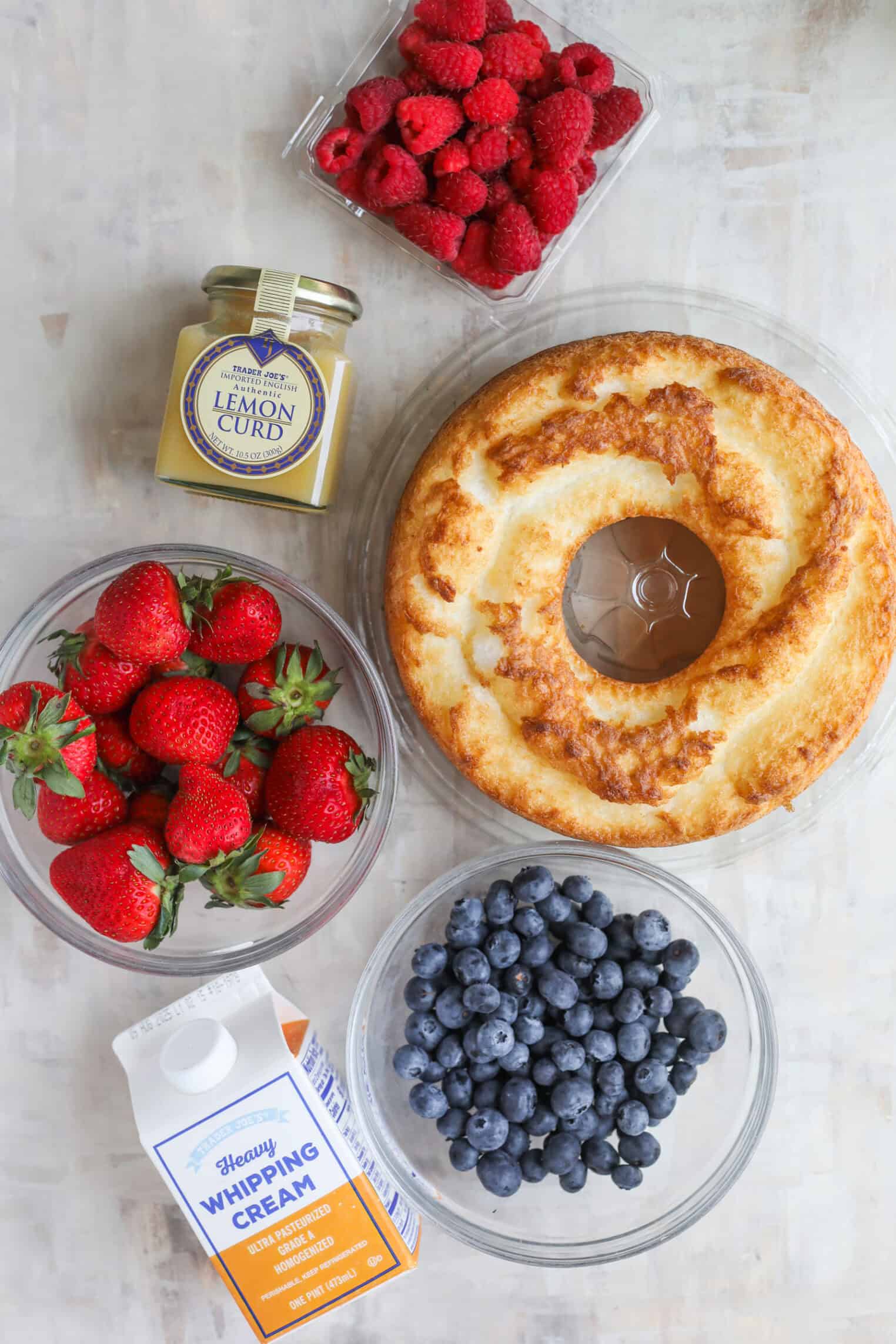 Fresh Berry Trifle 3 A Round Angel Food Cake, A Bowl Of Strawberries, Blueberries, Raspberries, Heavy Whipping Cream, And Lemon Curd Are Arranged On A Light Surface—Perfect Ingredients For Creating A Delightful Berry Trifle.