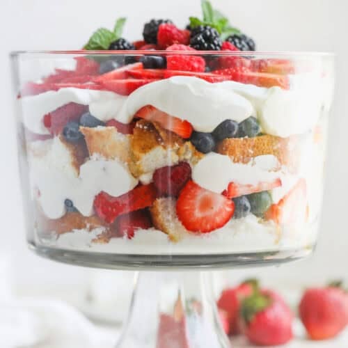 Fresh Berry Trifle 14 A Glass Trifle Bowl Filled With Layers Of Whipped Cream, Sponge Cake, Strawberries, Blueberries, And Blackberries Creates A Stunning Berry Trifle, Garnished With Fresh Berries And Mint. Two Strawberries Sit Beside The Bowl.