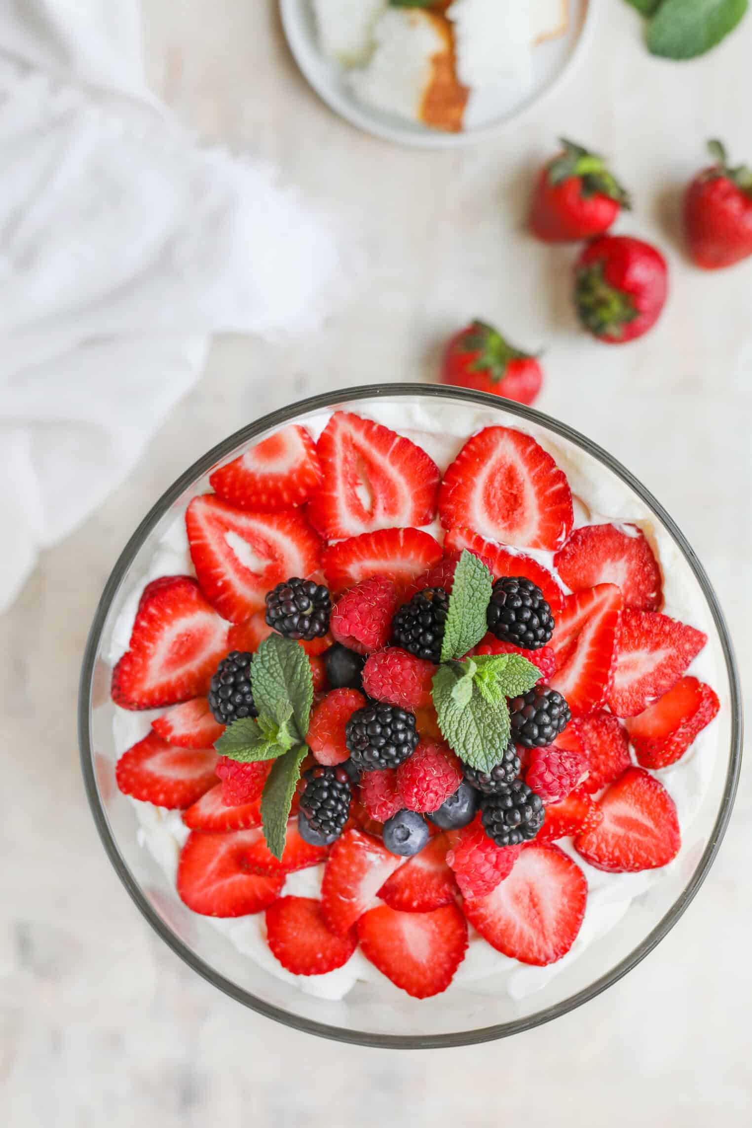 Fresh Berry Trifle 2 A Glass Bowl Filled With Whipped Cream, Topped With Sliced Strawberries, Blackberries, Blueberries, Raspberries, And Fresh Mint Leaves—This Berry Trifle Shines Beside Whole Strawberries And A Dessert Plate In The Background.