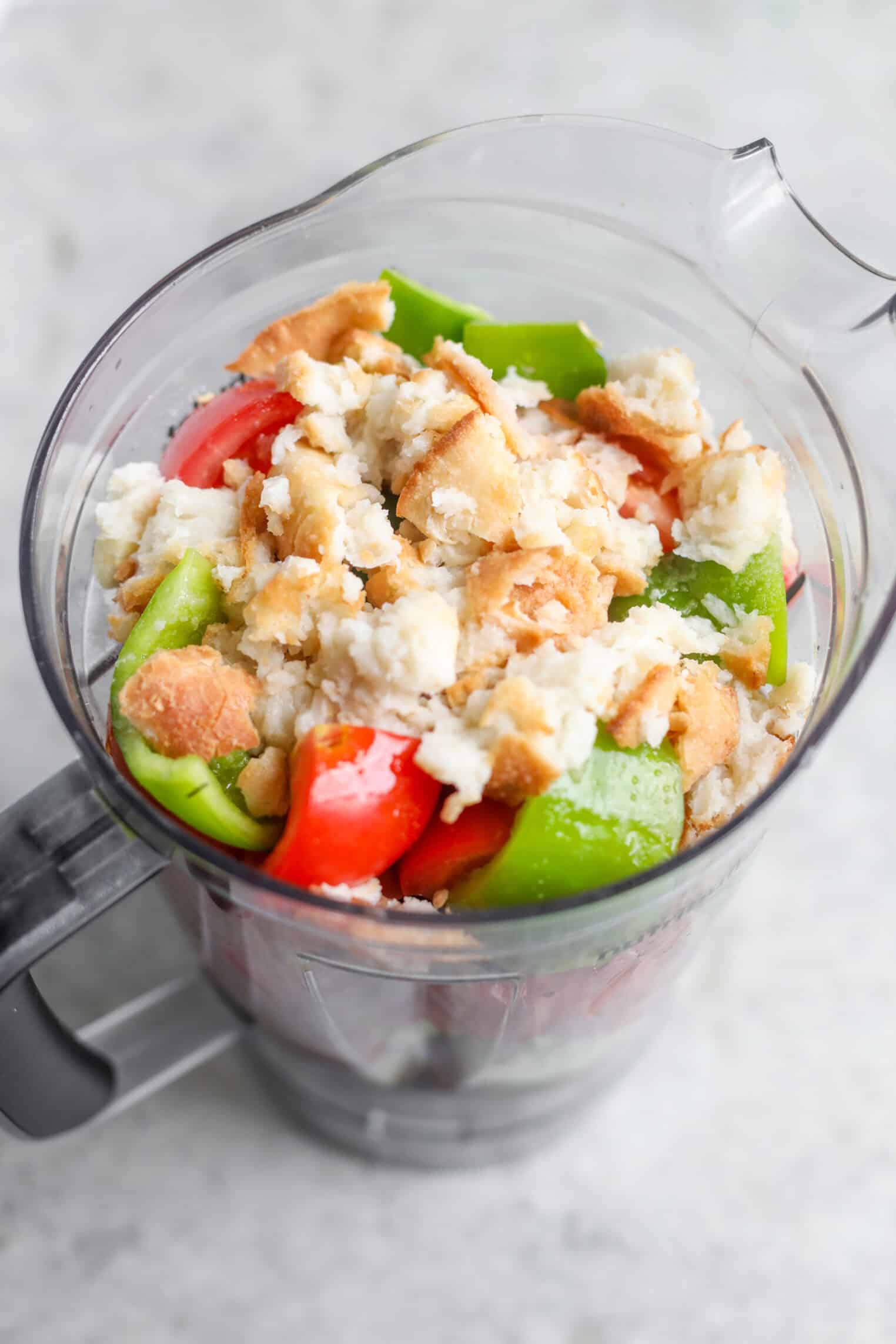 Gazpacho 8 A Blender Pitcher Filled With Chopped Green And Red Bell Peppers And Crumbled Bread Pieces, Perfect For Making Gazpacho, Sits On A Light-Colored Countertop.