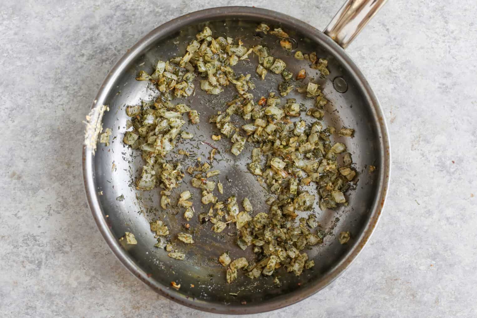 Greek Quinoa Zucchini Fritters 6 Chopped Onions And Herbs Sautéed In A Stainless Steel Skillet, Perfect As A Base For Quinoa Zucchini Fritters, Resting On A Light Gray Countertop.