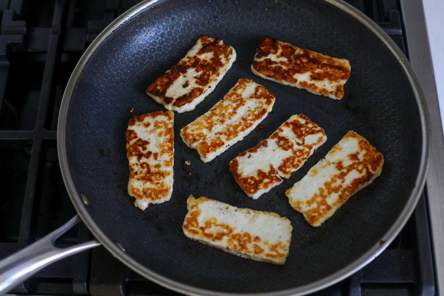 Halloumi Gyros 5 Slices Of Halloumi Cheese Being Pan-Fried In A Nonstick Skillet, Showing A Golden-Brown Sear On Each Piece—Perfect For Adding To Gyros. The Pan Is On A Stovetop.