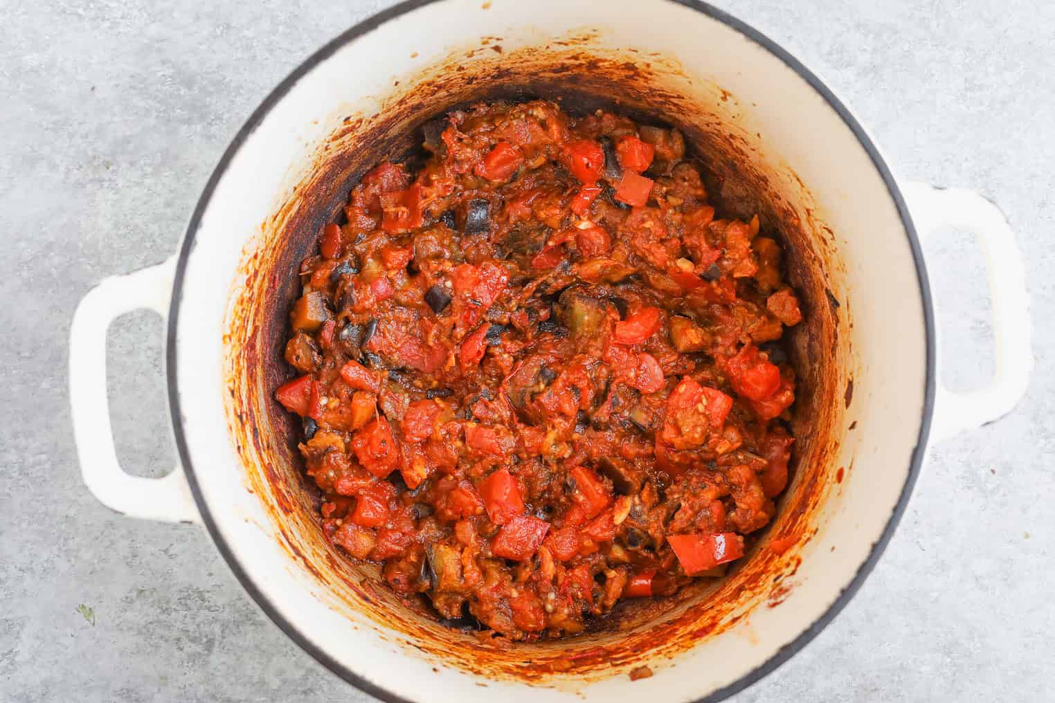A White Pot Filled With Cooked Ratatouille, Showing A Mixture Of Chopped Tomatoes, Eggplant, And Peppers In A Thick, Red Sauce. The Stained Sides Hint At Rich Flavor—Perfect Served Alongside Harissa Couscous.