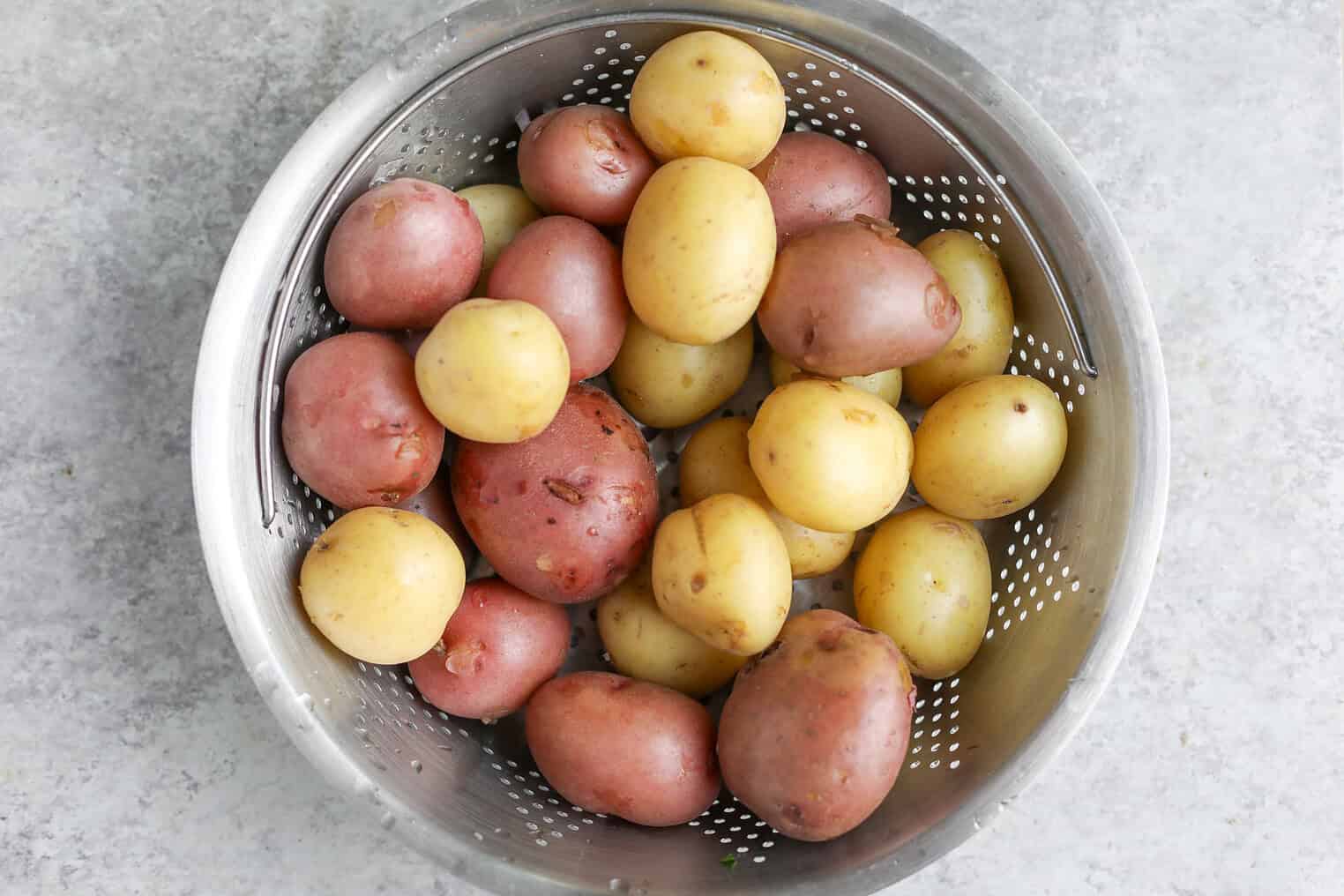 Creamy Herbed Potato Salad 5 A Metal Colander Filled With Washed Red And Yellow Baby Potatoes, Ready To Be Transformed Into A Fresh Herbed Potato Salad, Sits On A Light Gray Countertop.