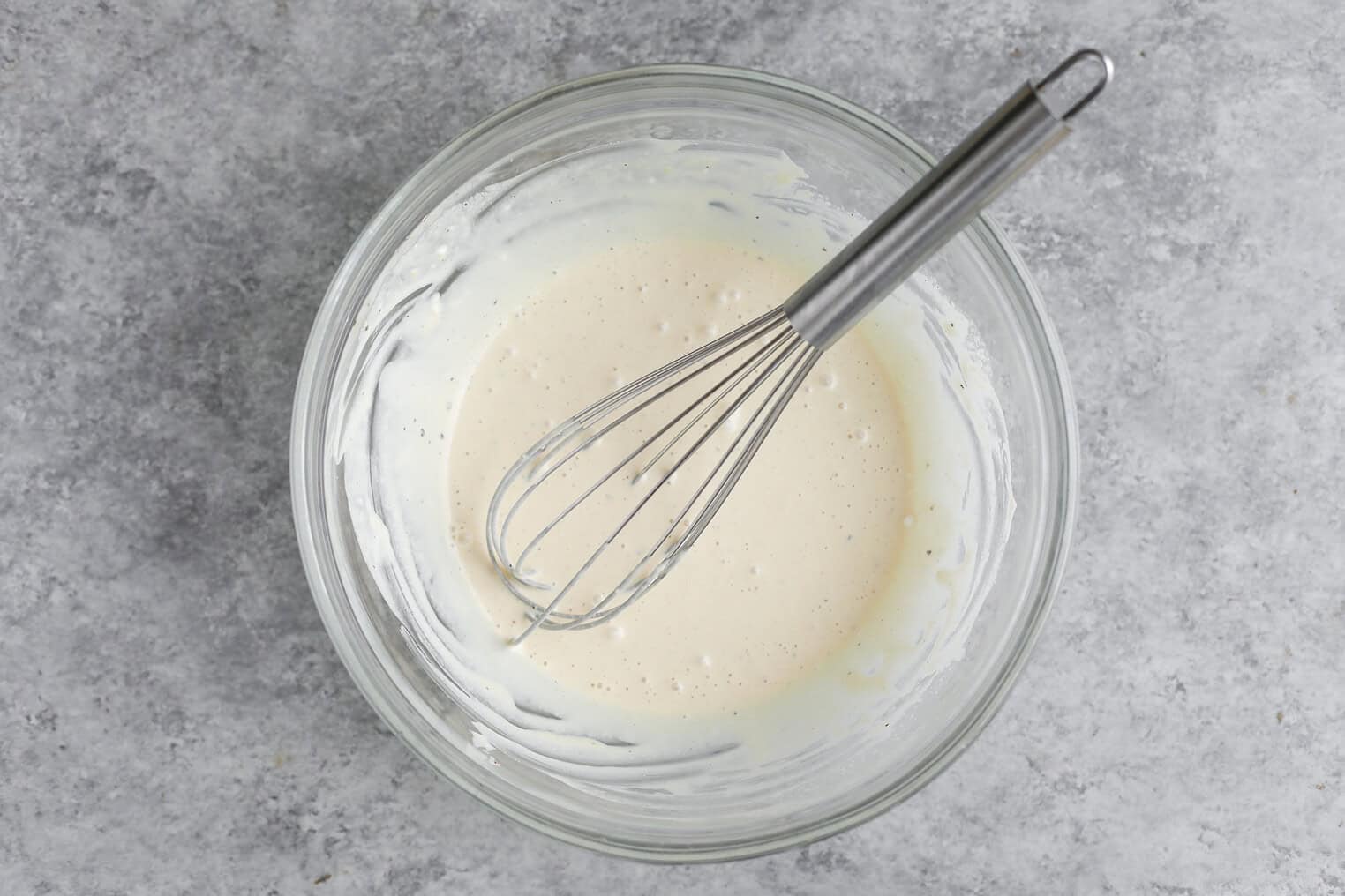 Creamy Herbed Potato Salad 6 A Glass Bowl Filled With Pancake Batter Being Mixed With A Metal Whisk, Placed On A Gray Textured Surface Next To A Serving Of Herbed Potato Salad.