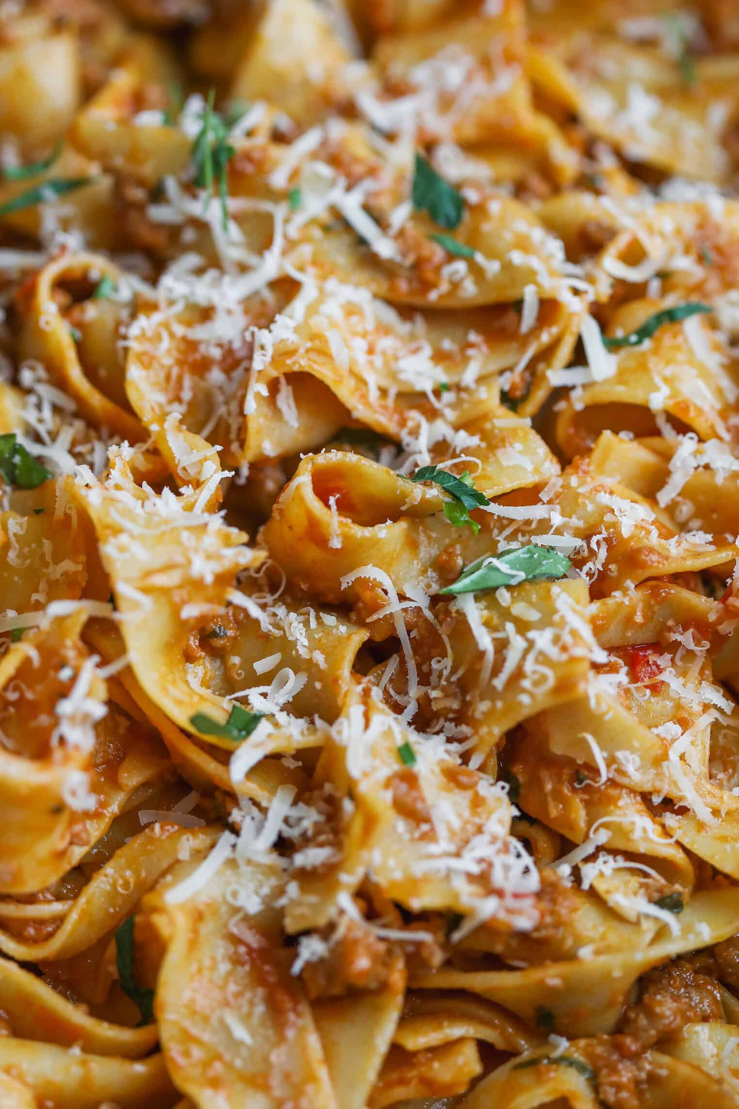 Close-Up Of Wide Ribbon Pasta Topped With A Creamy Plant-Based Bolognese Sauce, Grated Parmesan Cheese, And Fresh Basil Leaves. The Dish Appears Flavorful And Freshly Garnished.