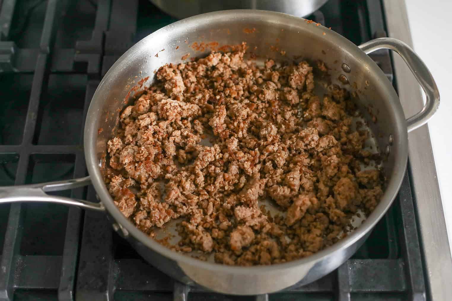 Ground Beef Is Being Browned In A Stainless Steel Pan On A Stovetop, With The Meat Broken Up Into Small Pieces And Some Browned Bits Visible—Just Like Prepping The Base For An Impossible Bolognese Or Vegan Pasta Dish.