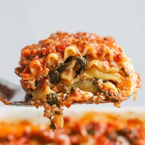 Impossible Lasagna 19 A Close-Up Of A Spatula Holding A Slice Of Cheesy Impossible Lasagna Above A Baking Dish Filled With More Lasagna, Showcasing Layers Of Pasta, Spinach, Tomato Sauce, And Melted Cheese.