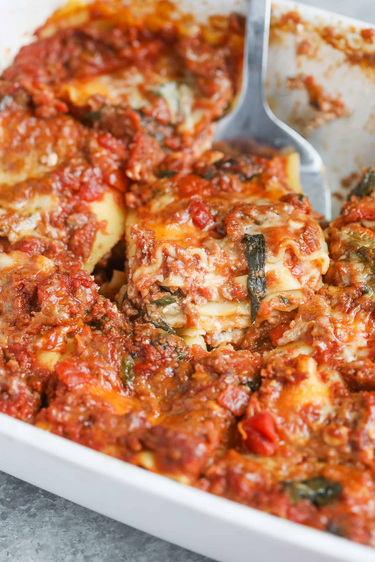 Impossible Lasagna 15 A Close-Up Of Impossible Lasagna In A White Dish, Showing Layers Of Pasta, Savory Plant-Based Meat Sauce, Melted Cheese, And Spinach, With A Serving Spatula Lifting A Portion.