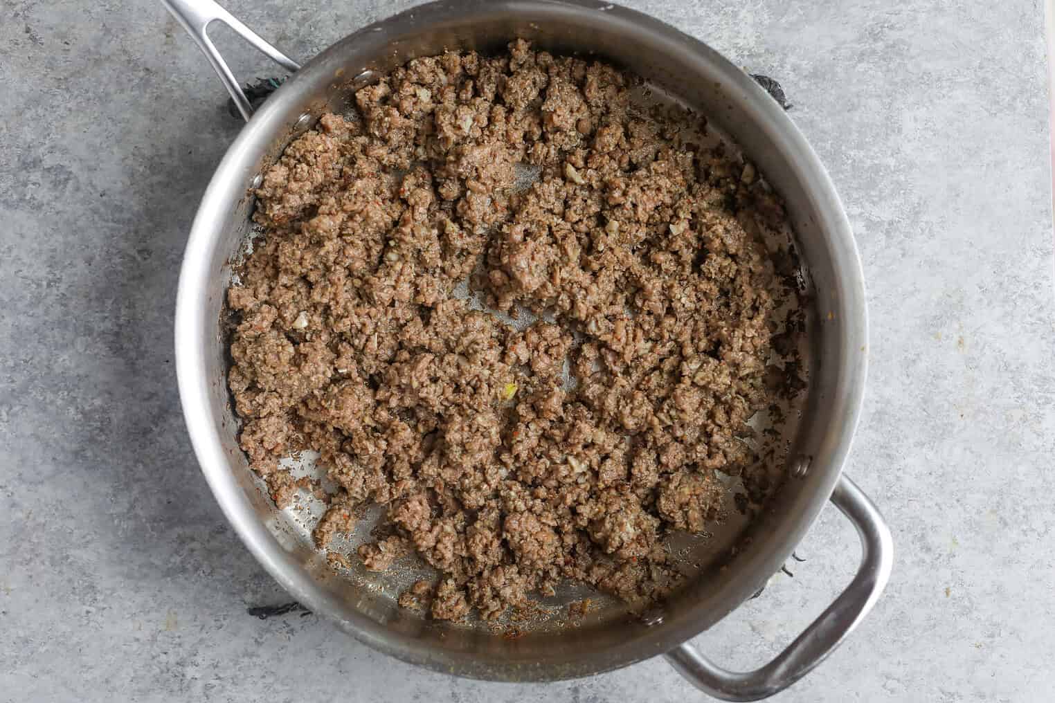 Impossible Lasagna 7 Cooked Ground Beef For Impossible Lasagna Sits In A Stainless Steel Skillet On A Gray Countertop. The Meat Is Browned And Crumbled, With Small Bits Visible Throughout The Pan.